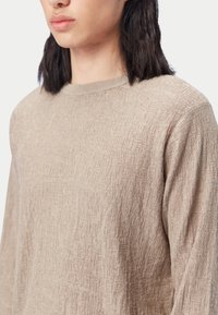 Beige tröja med långa ärmar i texturerat tyg, med ett diskret mönster och rund halsringning. Mjukt, lätt material.