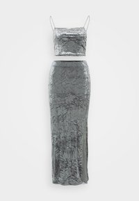 Metalický stříbrný dvoudílný outfit skládající se z topu s úzkými ramínky a přiléhavé dlouhé sukně se strukturovanými vzory.