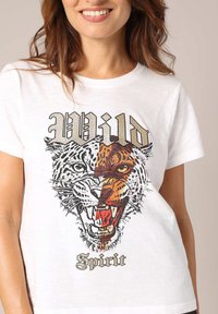 Witte katoenen t-shirt met een afbeelding van het gezicht van een tijger en een luipaard in felle kleuren, met de tekst "Wild Spirit" eronder in een gestileerd lettertype.