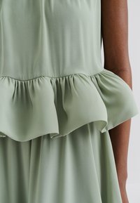 Svetlo zelena, lepršava bluzica z ruffled robom. Gladka tekstura, z nabranim pasom, ohlapen kroj in eleganten padec.