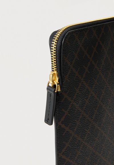 Κοντινό πλάνο μαύρου δερμάτινου θήκης με υφή, διακοσμημένη με καφέ σχέδιο διαμαντιού και χρυστό φερμουάρ με μαύρο δερμάτινο τριγωνικό τράβηγμα.