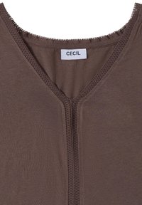 Chemise marron à col en V avec bordure en dentelle autour du col et bordure verticale au centre devant, avec une étiquette blanche portant le nom de la marque Cecil.