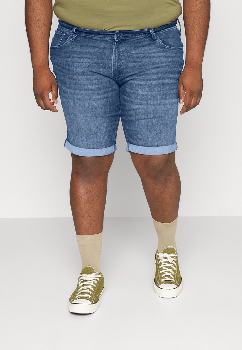 Blue denim shorts with rolled cuffs, a classic five-pocket design, worn with beige socks and green sneakers. Simple, casual fit.