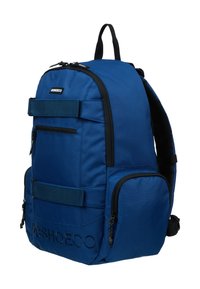 Blå tygryggsäck med rundad topp, flera dragkedjefack, svarta detaljer och en texturerad logotyp på framsidan. Justerbara axelremmar.