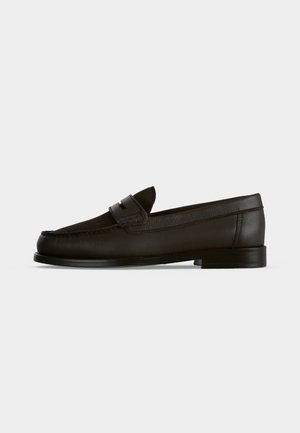 Mocassin penny en cuir noir avec petit talon, bout arrondi et détail de bride sur l’avant, vu de profil sur fond uni.