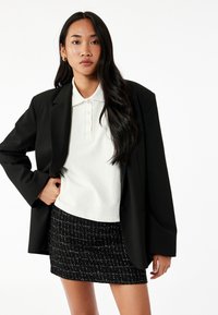 Sort oversized blazer, hvid polo skjorte med knapåbning og en sort tweed mini nederdel med et tekstureret mønster.