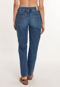 Jean en denim de bleu moyen avec une coupe droite, comportant deux poches arrière et une étiquette en cuir à la taille.