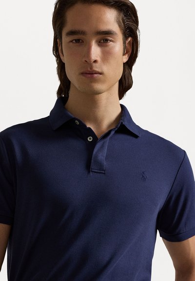 Navy blue polo shirt with short sleeves, a three-button placket, and a small embroidered logo on the left chest. Smooth fabric texture.