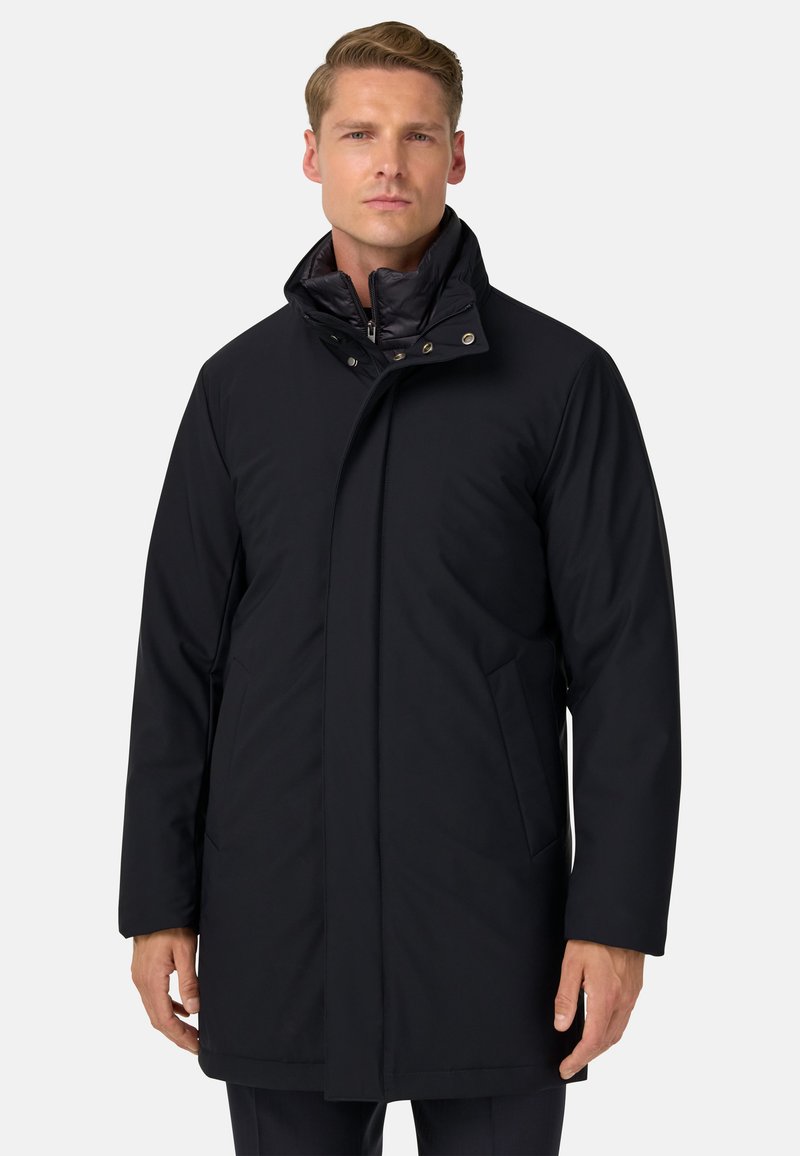 Abrigo acolchado negro con un alto cuello, con cierres a presión, bolsillos laterales y una textura mate suave. Diseño ajustado.