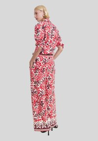 Bloemmotief outfit met een langetermijnshirt en wijde broek in rood, wit en bruin tinten. Getextureerde stof, getailleerde taille en gedetailleerde manchetten.