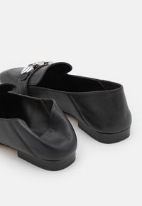 Scarpe in pelle nera con punta arrotondata e tacco basso e piatto. Presentano una fibbia decorativa in argento sulla tomaia e una superficie liscia.