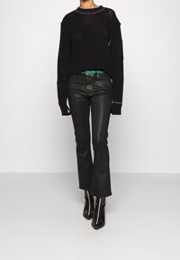 Suéter negro de punto con un corte holgado y un patrón texturizado, combinado con pantalones de campana negros. Los accesorios incluyen un cinturón verde y botas de tacón negras.