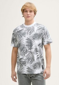 Camiseta de manga corta blanca con un patrón de hojas negras. Fabricada en algodón, con escote redondo y tejido texturizado. Etiqueta negra en el dobladillo.