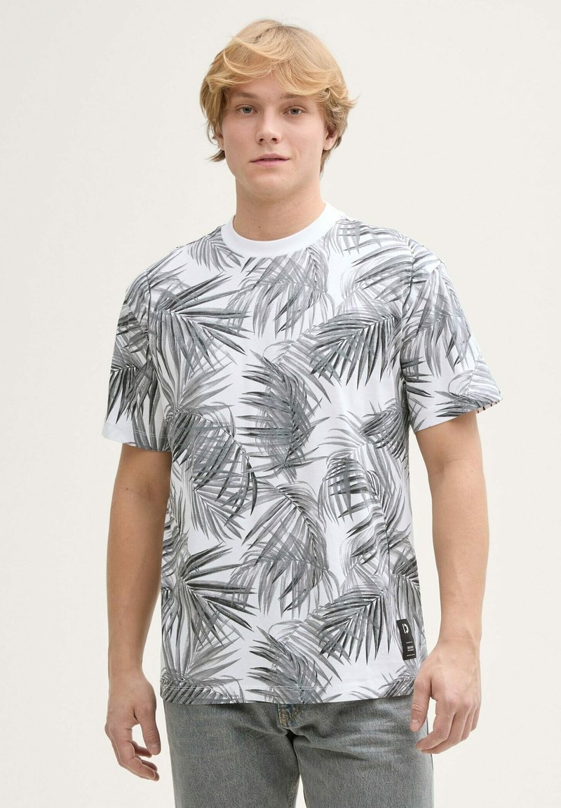 Camiseta de manga corta blanca con un patrón de hojas negras. Fabricada en algodón, con escote redondo y tejido texturizado. Etiqueta negra en el dobladillo.