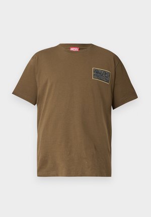 T-shirt en coton marron avec un col rond, comportant un patch graphique noir sur la poitrine gauche. Manches courtes et ourlet droit.