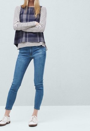 Haut à manches longues rayé bleu marine et blanc avec un motif à carreaux, associé à un jean skinny bleu clair et des chaussures blanches à semelles marron.