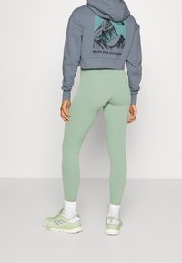 Felpa grigia corta con grafica di montagne e testo, abbinata a leggings verde menta e scarpe da ginnastica verde chiaro.