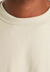 Pull beige à col rond avec col côtelé, texture douce et design minimaliste, adapté pour une tenue décontractée.