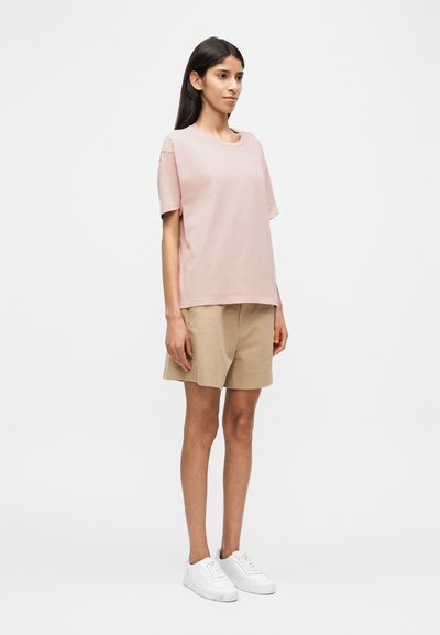 Ροζ βαμβακερό μπλουζάκι με κοντά μανίκια και στρογγυλή λαιμόκοψη, συνδυασμένο με μπεζ βαμβακερά σορτς και λευκά αθλητικά παπούτσια. Απλή, άνετη εφαρμογή.