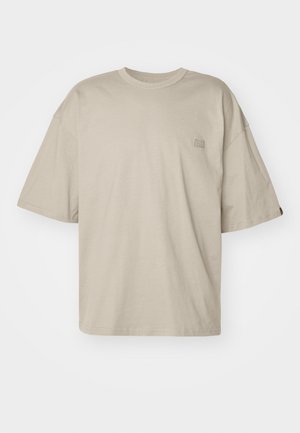 Beige oversized t-shirt i bomull, med rund halsringning och korta ärmar, och en liten logotypdetalj på vänster bröst.