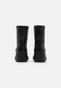 Botines de cuero negro con un acabado texturizado, puntera cuadrada, tacón bajo en bloque y una tira en la parte trasera para facilitar su uso.