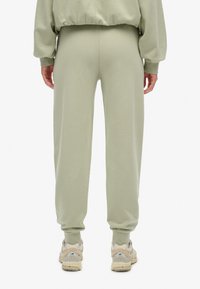 Lysgrønne sweatpants med en afslappet pasform, tapered cuffs og blød tekstur, parret med lyse sneakers med en tekstureret sål.