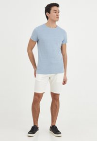 Lyseblå t-skjorte med korte ermer, rund hals, kombinert med hvite shorts og svarte joggesko. Løs passform med brettede ermer og rene linjer.
