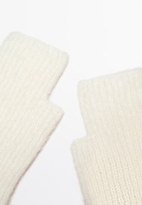 Guanti senza dita realizzati in morbido materiale a maglia di colore crema, con una texture a coste, dotati di estremità aperte per le dita e un aspetto accogliente.
