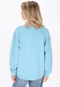 Ljusblå oversized sweatshirt med rund halsringning, sänkta axlar och ribbade ärmmuddar. Mjuk tyg och avslappnat design, lämplig för lager-på-lager stil.
