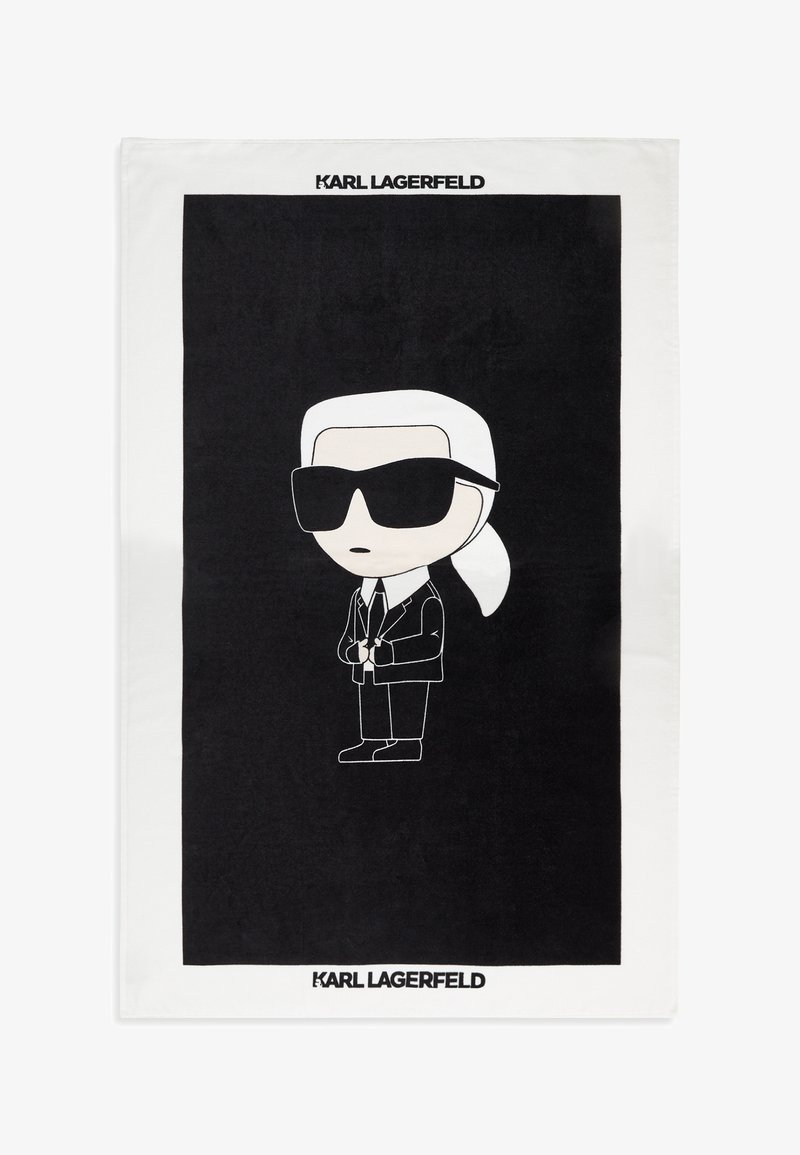 Figure de dessin animé aux cheveux blancs en queue de cheval, lunettes de soleil noires, costume noir et cravate centrée sur un fond noir avec le texte "KARL LAGERFELD" en haut et en bas.
