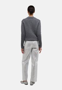 Pull gris en tricot avec un col rond, associé à un pantalon large métallisé argenté. Porté avec des chaussures plates scintillantes. Vue de dos.