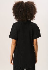 Black pleated top featuring a collared neckline, short sleeves, and a rounded hem with textured fabric for depth.