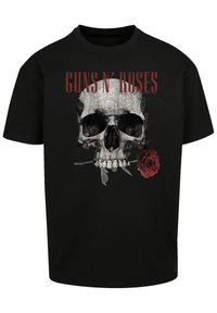 Camiseta de algodón negra con un gráfico de una calavera gris con una rosa roja y el texto "GUNS N’ ROSES" en rojo por encima del diseño. Manga corta.