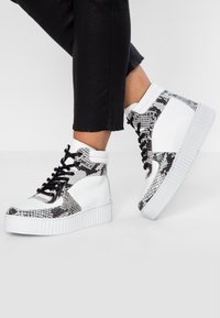 Höga sneakers med en vit läderbas och svarta ormskinnsmönstrade detaljer, tjock vit sula och svarta snören.