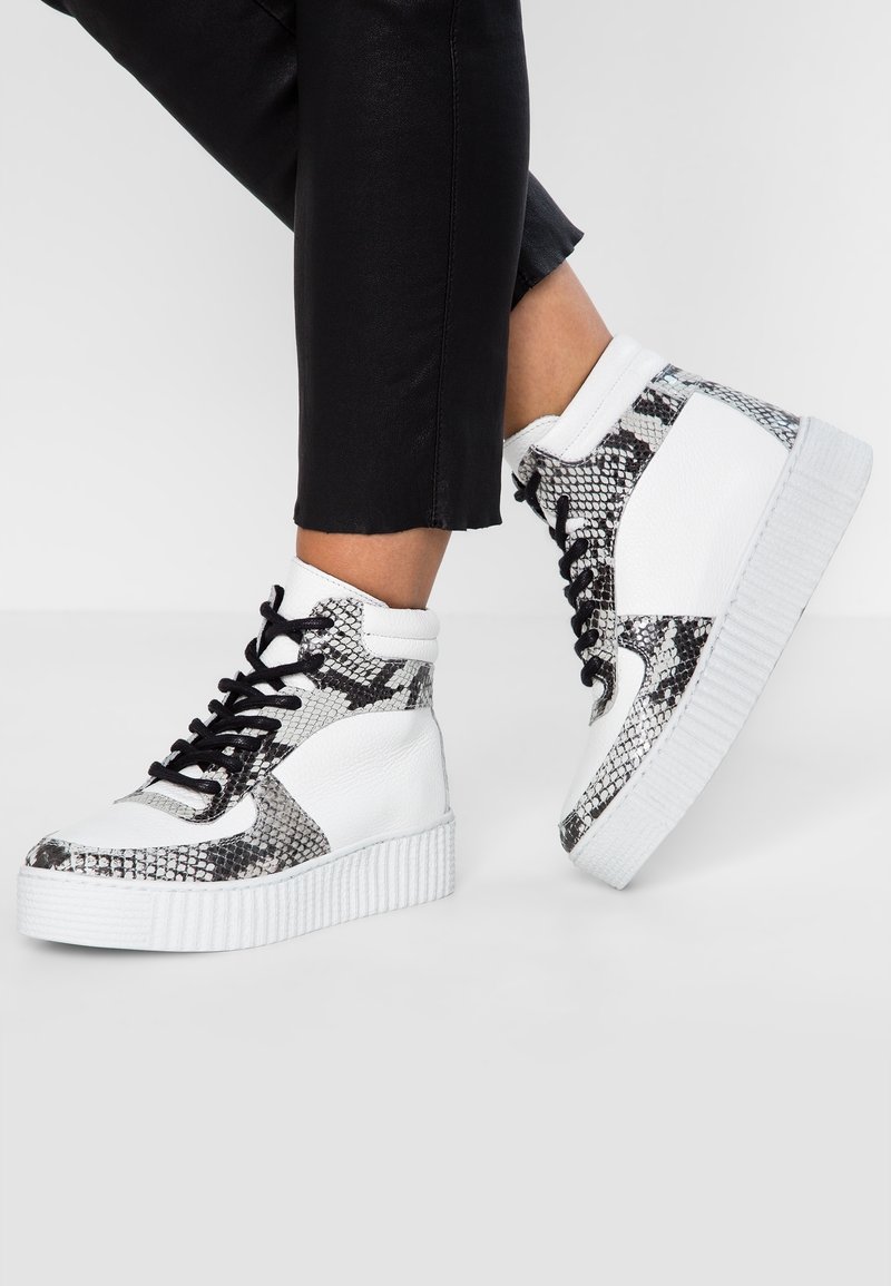 Höga sneakers med en vit läderbas och svarta ormskinnsmönstrade detaljer, tjock vit sula och svarta snören.