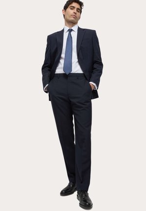 Marineblauer Anzug mit maßgeschneiderter Passform, weißem Hemd und blauem, strukturiertem Krawatte. Schwarze Lederschuhe vervollständigen das Outfit.