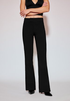 Zwarte uitlopende broek van gladde stof met een nauwsluitende taille, voorzien van een strak vooraanzicht en gecombineerd met zwarte puntige schoenen.