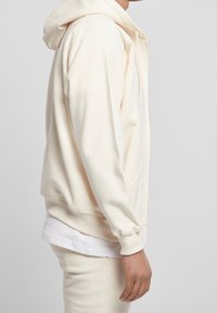 Ljus crème hoodie med känguruficka, dragsko på huvan och ribbad mudd. Kombinerad med en vit undertröja och matchande byxor.