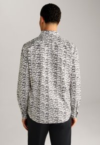 Langärmliges Hemd mit einem weißen und schwarzen Muster aus abstrakten Formen, hergestellt aus leichtem Stoff mit klassischem Kragen und Knopfmanschetten.