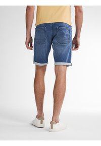 Shorts di denim di colore blu scuro con una finitura sbiadita, orli arrotolati, tasche posteriori, abbinati a sneakers bianche con dettagli beige.