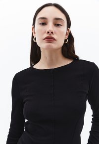 Musta pitkähiha toppi, jossa on pyöreä pääntie, tekstuuri kankaassa sauman yksityiskohdilla ja vartalonmyötäinen muotoilu. Sileä pinta koko ajan.