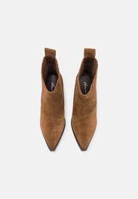 Un paio di stivaletti marroni in suede con punta affusolata e linguette per il pattino, visti dall'alto su uno sfondo bianco uniforme.