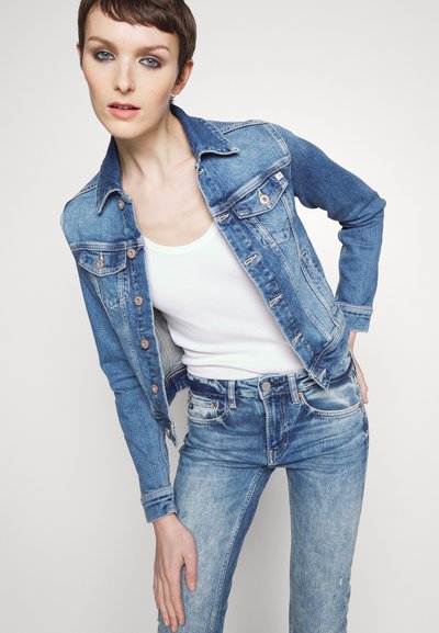 Veste en jean bleu clair avec une coupe classique, des boutonnages et des poches poitrine. Associée à un jean délavé assorti et un débardeur blanc.