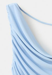 Tissu bleu clair avec plusieurs plis horizontaux et une fine bretelle sur fond blanc.