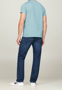 Svetle modrá košile s krátkým rukávem, tmavě modré džíny a bílé tenisky. Košile má kulatý výstřih, džíny mají zadní kapsy.