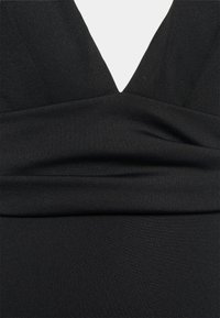 Musta mekko, jossa on syvä V-aukko, jämäkkä bodice kerättyine kankaineen sekä sileä ja joustava kangas.