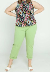 Färgglad mönstrad ärmlös topp med svart bakgrund, i kombination med ljusgröna byxor med uppvikta ärmar och vita sandaletter med öppen tå.