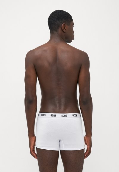 White cotton boxer briefs with a fitted design and black elastic waistband featuring "GCDS" logo repeated. Smooth texture, mid-thigh length.