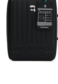 Czarna walizka Karl Lagerfeld z wytłoczonym logo, przypinka z cartoonową twarzą w okularach przeciwsłonecznych i białymi włosami oraz czarna zawieszka bagażowa z białym tekstem.