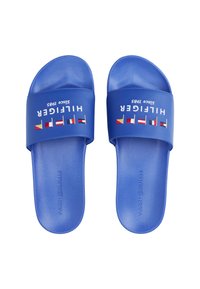 Niebieskie sandały wsuwane z teksturowanym wzorem. Posiadają szeroki pasek z napisem "HILFIGER" w białym kolorze oraz haftowaną flagę. Gładkie podeszwy.